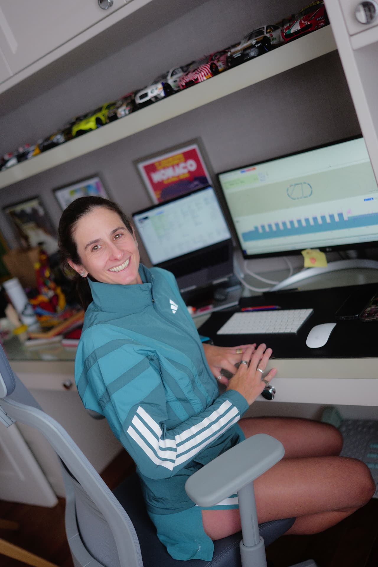Ana Paula sorrindo à mesa do escritório, com telas de gráficos e dados de treino