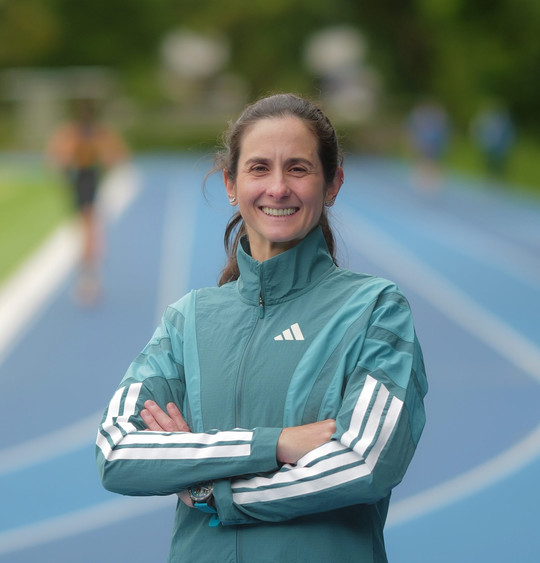 Ana Paula sorrindo, de braços cruzados, em uma pista de atletismo azul